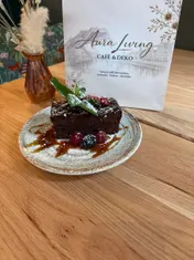 Brownie mit Minze, Erdbeere, Himbeeren, Brombeere, Puderzucker und Karamellsauce auf einem gesprenkelten Teller, dahinter die Karte von Aura Living