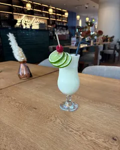 Bar mit beleuchtetem Aura-Living-Schriftzug, Pendelleuchten und Kronleuchter, im Vordergrund eine Pina Colada