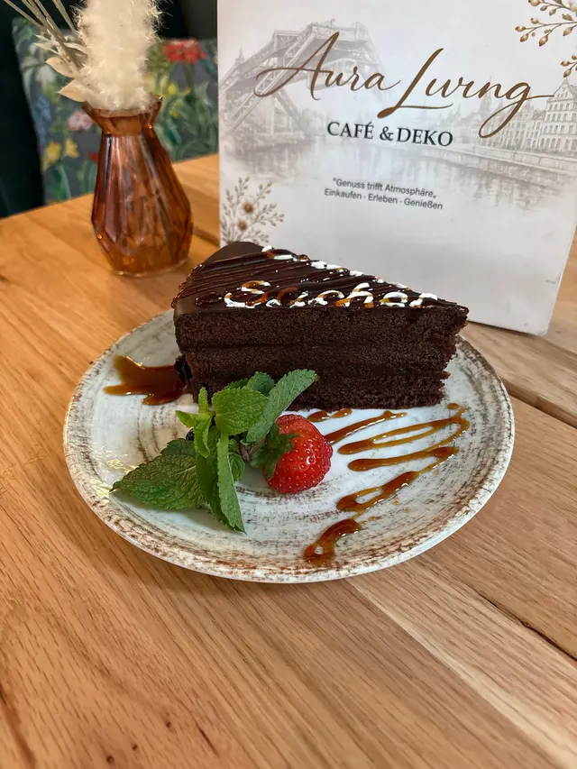 Stück Schokoladentorte mit Schriftzug „Sacher“ aus weißer Glasur, garniert mit Minze, Erdbeere und Karamellsauce