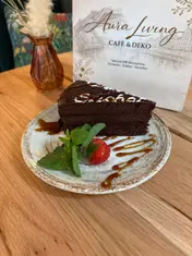 Stück Schokoladentorte mit Schriftzug „Sacher“ aus weißer Glasur, garniert mit Minze, Erdbeere und Karamellsauce