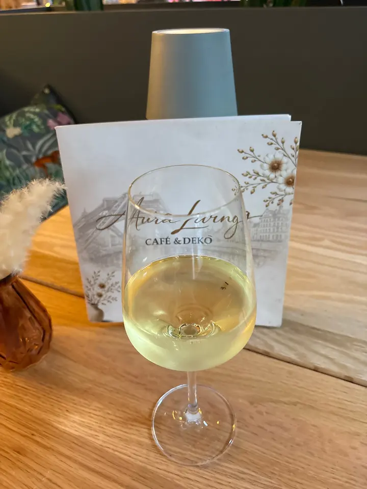 Glas Weißwein auf einem Holztisch vor der aufgestellten Karte von Aura Living