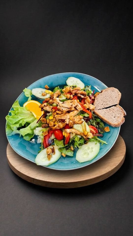 Grilled Chicken Salad auf einer Eichenplatte vor dunklem Hintergrund
